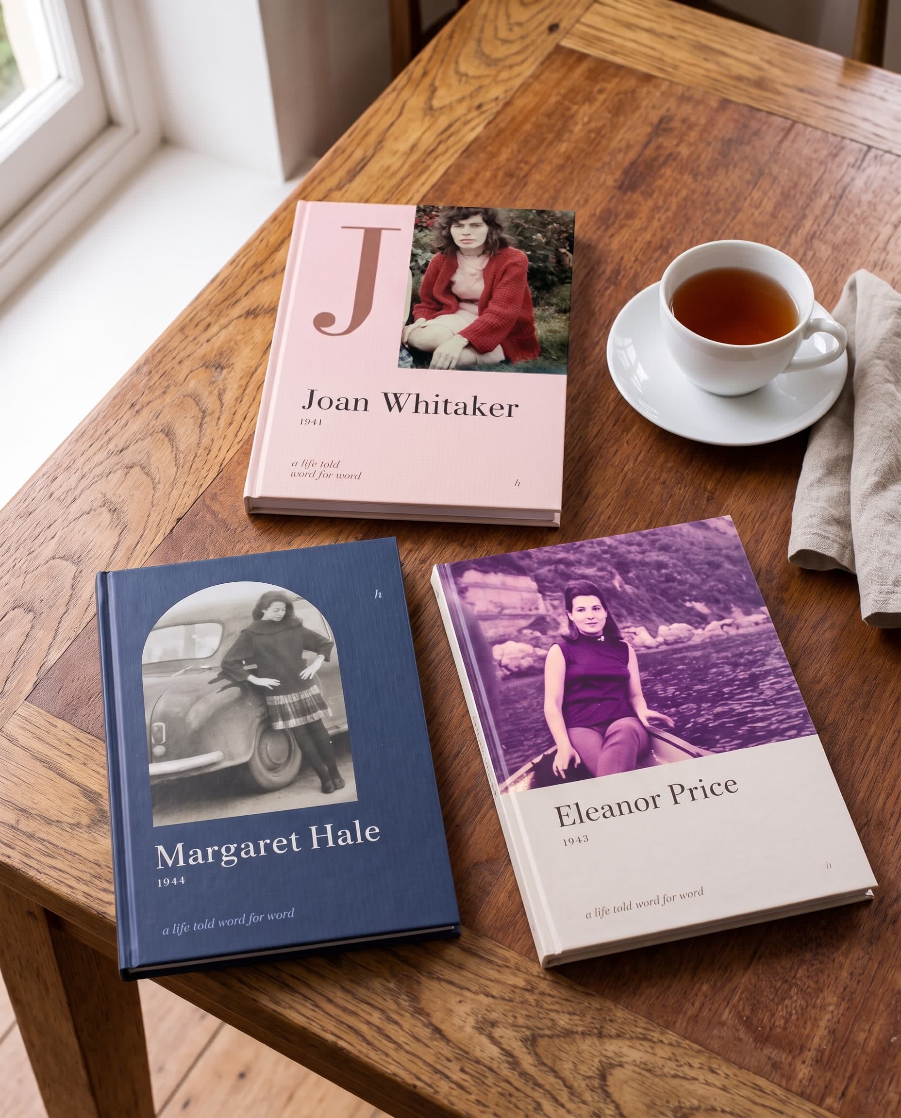 Three slim hardcover memoir books with old family photos on their covers, lying on a wooden table next to a cup of tea. AI-generated image.
